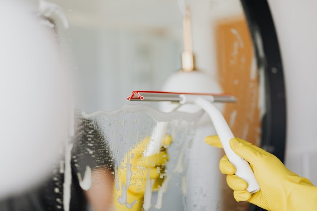 Person using a squeegee to clean a foamy bathroom mirror indoors.